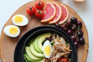 A vibrant, healthy salad bowl with avocado, eggs, tomatoes, grapefruit, and cherries on a wooden board.